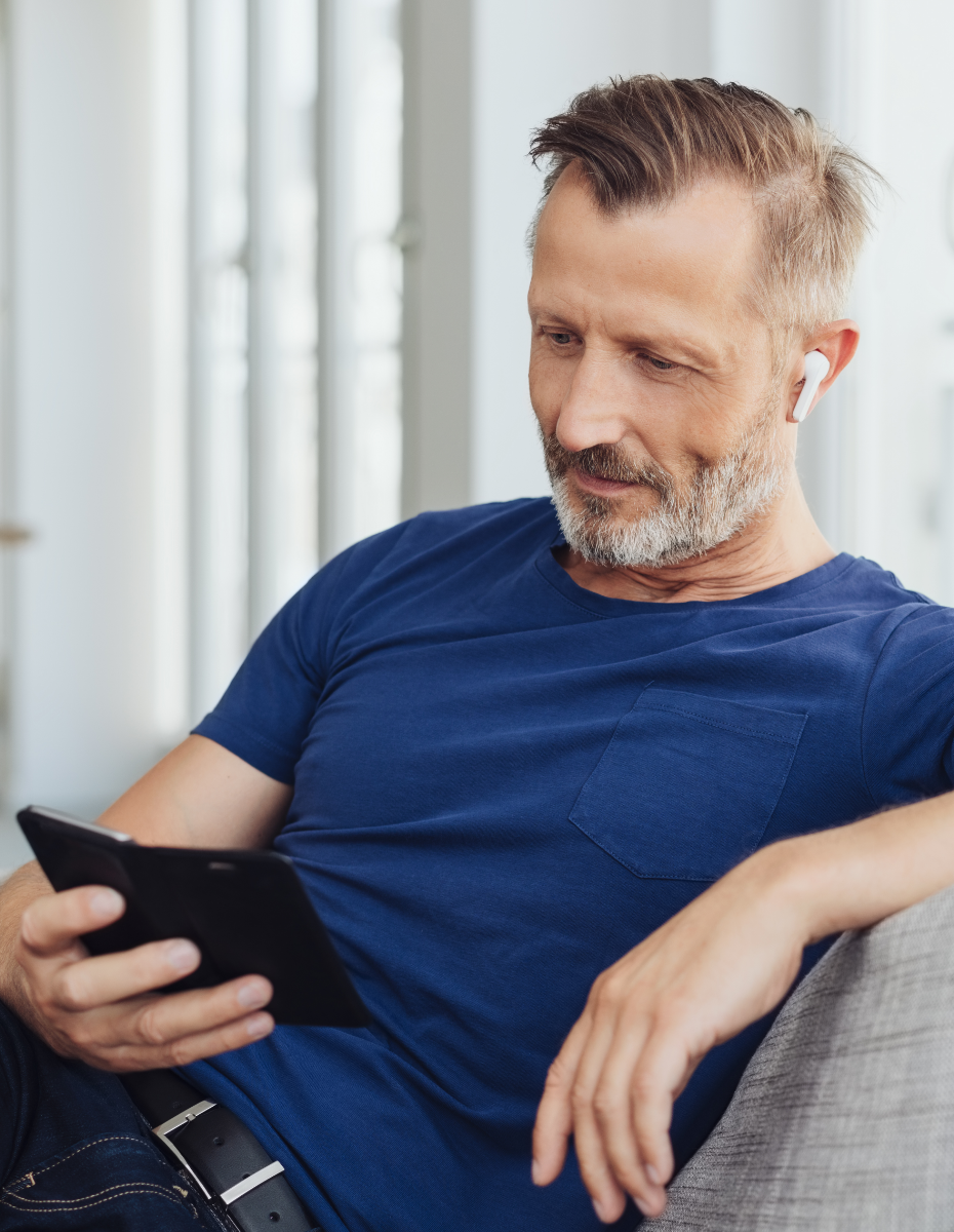 Mann mit Kopfhörer auf dem Sofa mit Blick ins Smartphone.